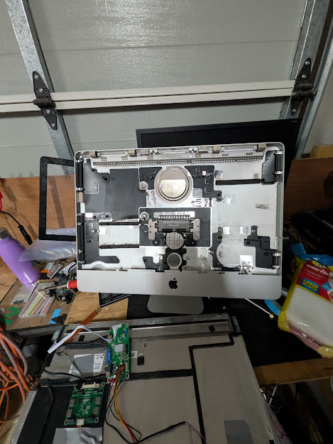 iMac shell laid face-down on a workbench, rear case removed, logic board and internals stripped out showing the empty aluminium chassis