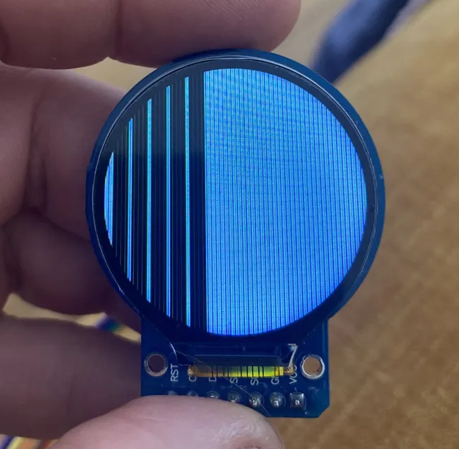 Defective GC9A01 round TFT display showing vertical blue lines instead of correct output, held in hand