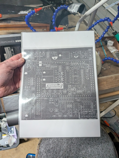 Printed Speeduino v0.4.4b schematic held up showing the full board layout and component references